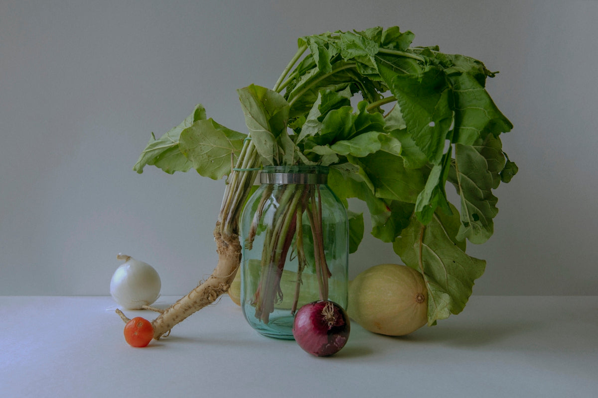 a glass vase filled with greens and vegetables